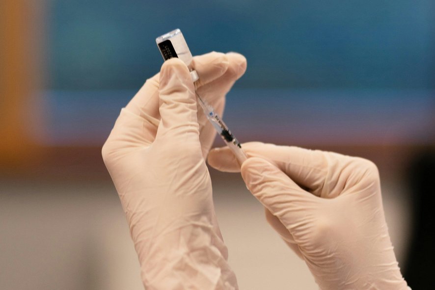 zwei Hände mit Hygienehandschuhen ziehen eine Spritze auf